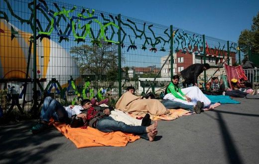 Migrants lay on the ground at the entrance of a migrant and refugee camp near Porte de la Chapelle, northern Paris, on April 19, 2017