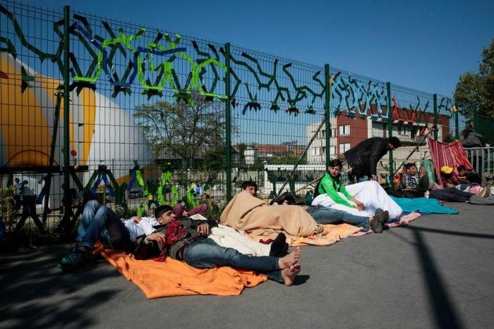 Migrants lay on the ground at the entrance of a migrant and refugee camp near Porte de la Chapelle, northern Paris, on April 19, 2017