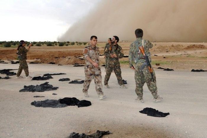 Fighters from the Syrian Democratic Forces (SDF) walk along a road dotted with black veils ditched by women after they crossed over from Islamic State group territory near Tishreen Farms, on the northern outskirts of Raqa on May 2, 2017