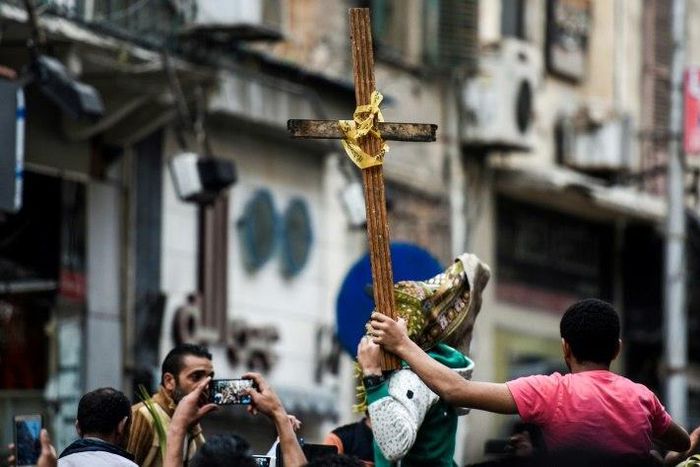 Egyptians raise a wooden cross and palm leaves as they gather outside the Coptic Christian patriarchate in the Mediterranean city of Alexandria where a jihadist bombing killed 17 people