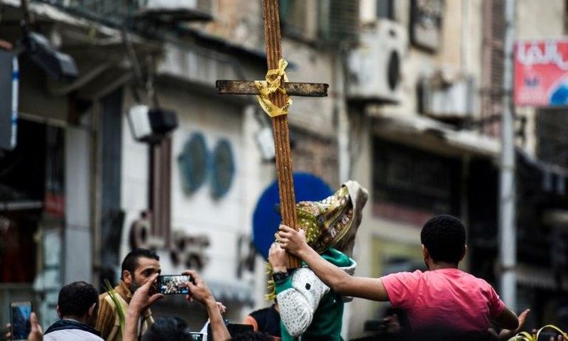 Egyptians raise a wooden cross and palm leaves as they gather outside the Coptic Christian patriarchate in the Mediterranean city of Alexandria where a jihadist bombing killed 17 people