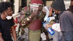 A protester offers water to a riot police officer overwhelmed by teargas during protests outside The Nation Centre building, Nairobi on June 25, 2024