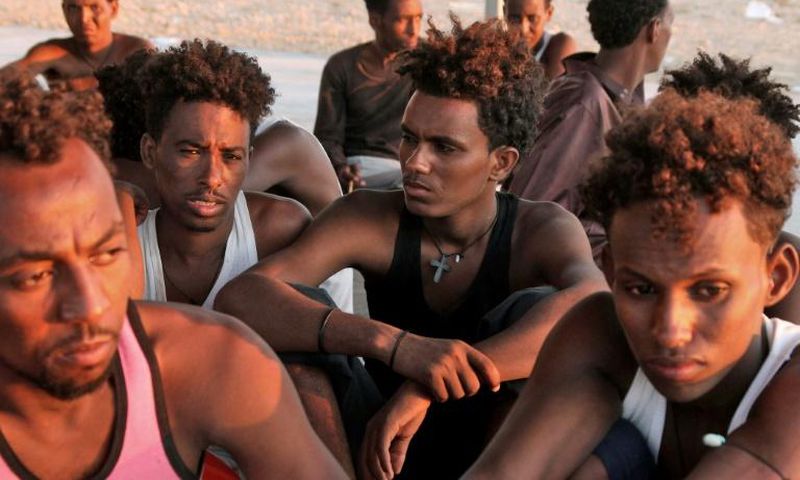 Rescued migrants sit on the coast in the fishing village of Khoms, east of the Libyan capital