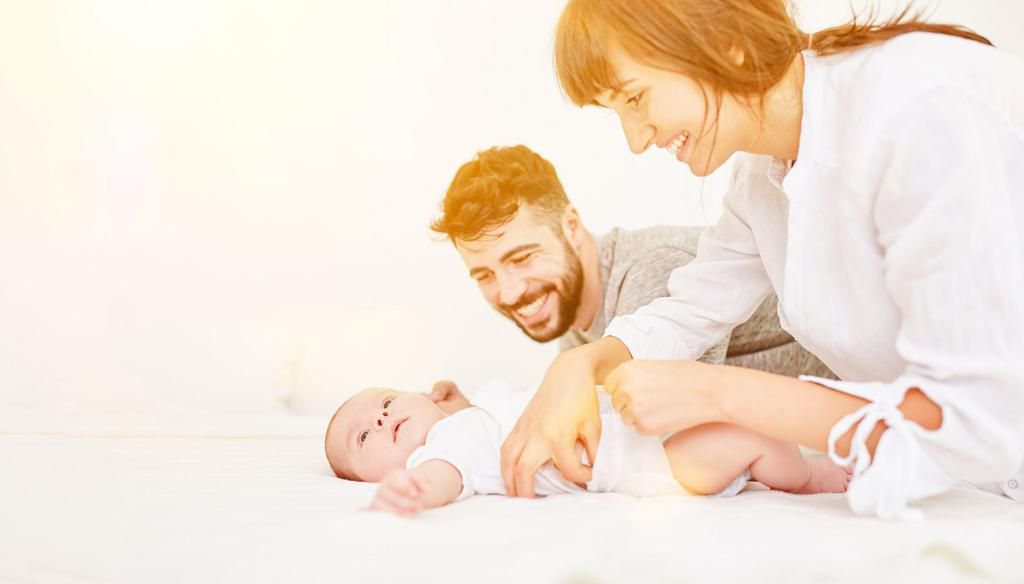 Happy Parents Playing With Son On Bed At Home