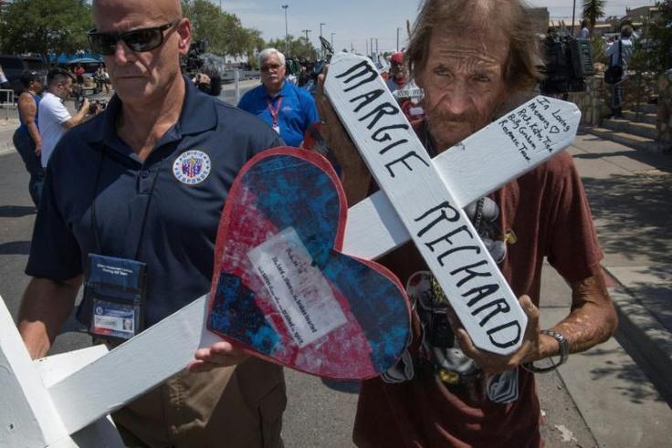 Antonio Basco (R) holds the cross of his common-law wife Margie Reckard who died in the El Paso shooting, as he walks to a makeshift memorial after the shooting that left 22 people dead