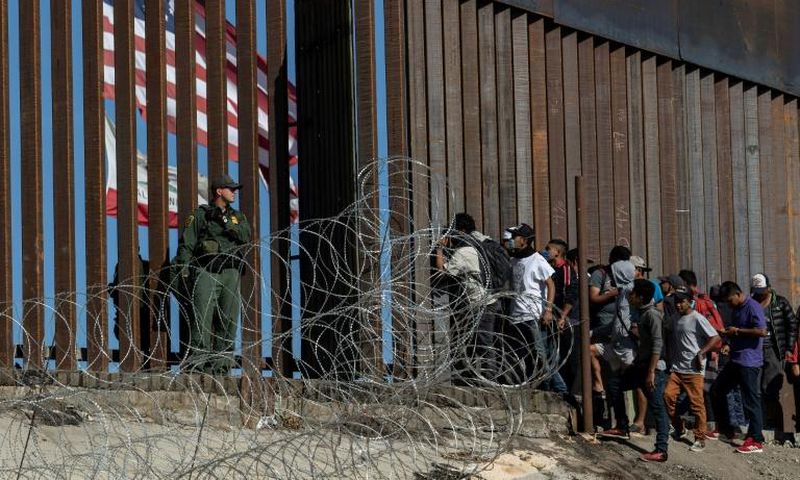 Central American migrants look through a border fence as a US Border Patrol agent stands guard near Tijuana, Mexico: people who cross the border illegally will have their DNA collected by US officials in the future