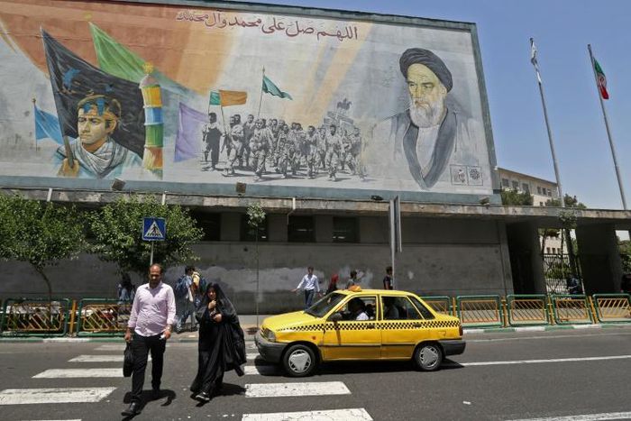 Iranians walk under a mural of Ayatollah Ruhollah Khomeini, who remains a guiding figure in the country 30 years after his death