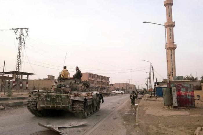 Members of the pro-Syrian government forces ride on a tank as it drives down a street in the Syrian border town of Albu Kamal