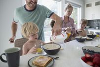 Father pouring milk into cereal for son at breakfast