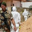 A Lebanese army soldier walks past military intelligence forensic investigators ar the scene where two drones came down in the vicinity of a media centre of the Shiite Hezbollah movement