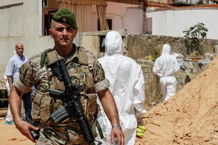 A Lebanese army soldier walks past military intelligence forensic investigators ar the scene where two drones came down in the vicinity of a media centre of the Shiite Hezbollah movement