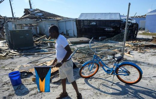 Irvin Russell carries the Bahamian flag as he walks past a damaged truck on Treasure Cay in the hurricane-hit Bahamas