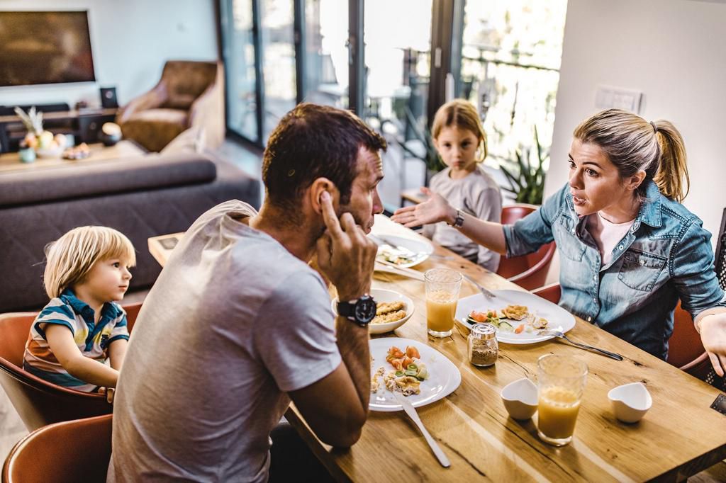 Young parents arguing while having lunch with their kids at home.