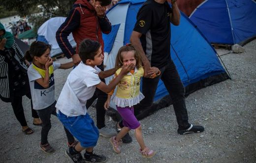 Migrants shield their mouths from tear gas during clashes at the Moira refugee camp