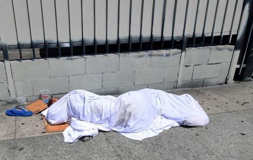 A homeless person' sleeping under a sheet on a sidewalk in Los Angeles, California on August 22, 2019, home to one of the nation's largest homeless populations
