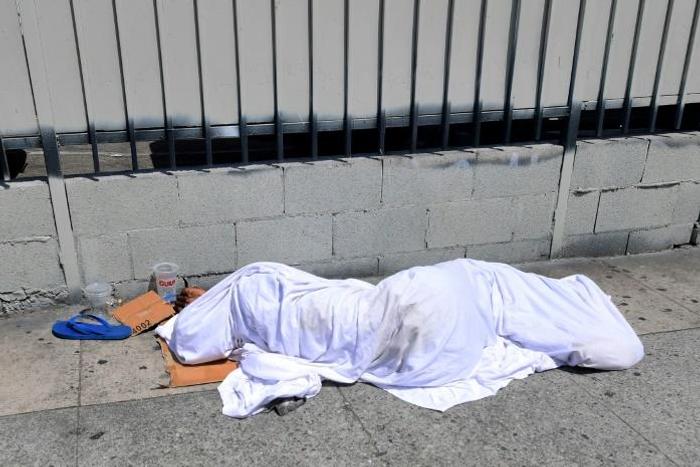 A homeless person' sleeping under a sheet on a sidewalk in Los Angeles, California on August 22, 2019, home to one of the nation's largest homeless populations