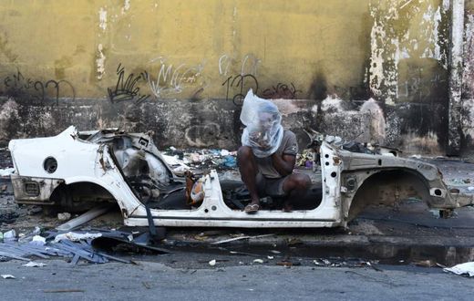 A drug user smokes crack beside the shell of a burnt out car in the Sem Terra favela in Complexo da Mare, Rio de Janeiro, on April 29, 2019