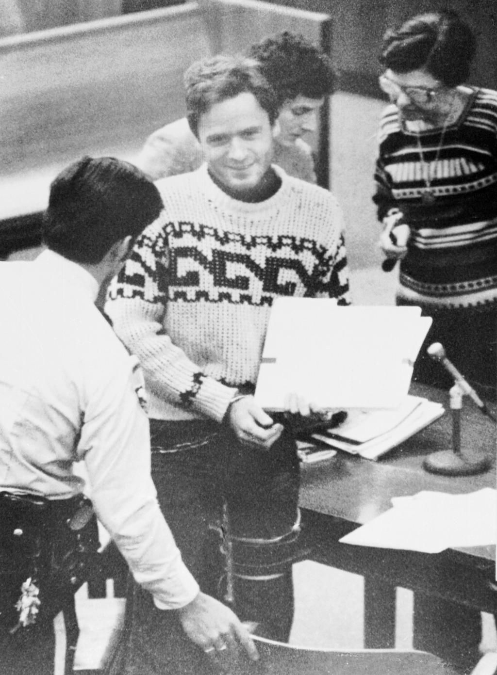 Ted Bundy looking rather happy as he enters court with legal files in hand.