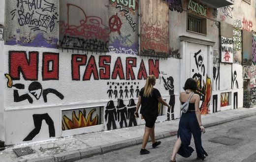 Women walk past a recent graffiti in Athens' historic district of Exarchia