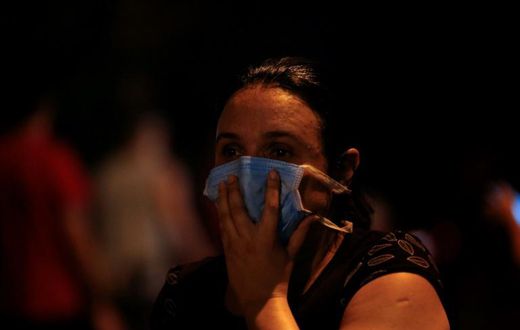 A woman covers her face with a surgical mask to protect herself from the smoke during a fire at the Badim hospital in Rio de Janeiro