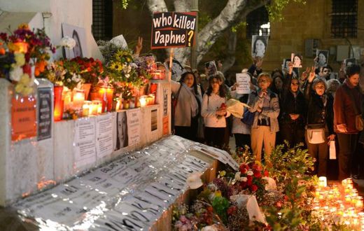 People hold portraits as they stand beside lighted candles placed in memory of murdered journalist Daphne Caruana Galizia on the sixth month anniversary of her death at a makeshift memorial outside the law courts in Valletta, Malta on April 16, 2018