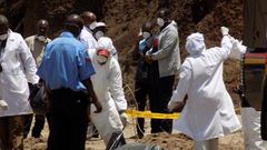 Detectives stabd next to the body of murdered Catholic priest Michael Kyengo