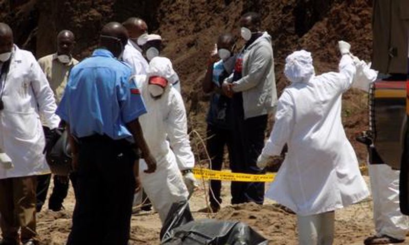 Detectives stabd next to the body of murdered Catholic priest Michael Kyengo