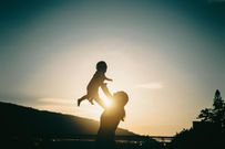 Silhouette of mother raising baby girl in the air outdoors against sky during a beautiful sunset