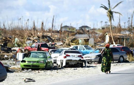 A woman walks by destroyed cars in The Mudd neighborhood of Marsh Harbour