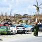 A woman walks by destroyed cars in The Mudd neighborhood of Marsh Harbour