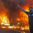 A protester flashes the V for victory sign as a riot police vehicle burns behind him during clashes amidst demonstrations against state corruption, failing public services, and unemployment in the Iraqi capital