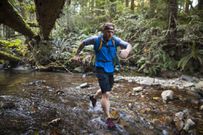 Man trail running across stream in forest near Elbow Lake in Fraser Valley, Harrison Mills, British Columbia, Canada