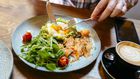 Man eating avocado toast with egg, salmon and arugula salad for brunch at the restaurant
