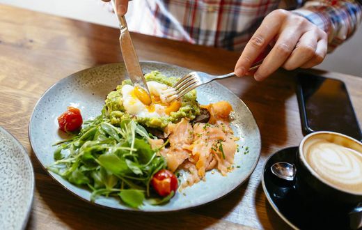 Man eating avocado toast with egg, salmon and arugula salad for brunch at the restaurant