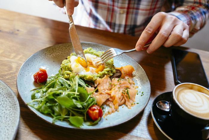 Man eating avocado toast with egg, salmon and arugula salad for brunch at the restaurant