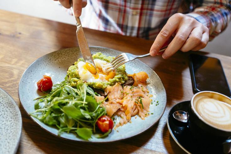Man eating avocado toast with egg, salmon and arugula salad for brunch at the restaurant