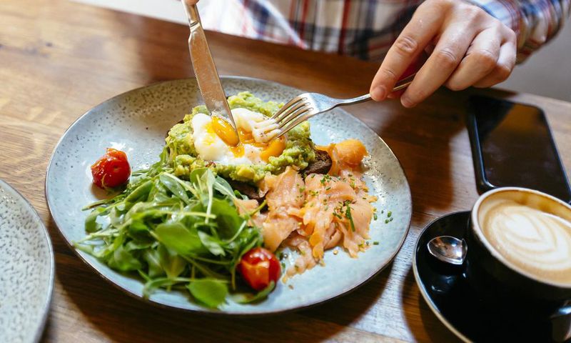 Man eating avocado toast with egg, salmon and arugula salad for brunch at the restaurant