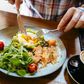 Man eating avocado toast with egg, salmon and arugula salad for brunch at the restaurant