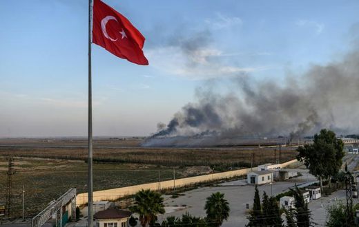Smoke rises from the Syrian town of Tal Abyad, in a picture taken from the Turkish side of the border where the Turkish flag is seen in Akcakale on October 10, 2019, on the second day of Turkey's military operation against Kurdish forces