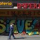 A man walks past a boarded up shoe store in valparaiso with graffiti that reads "Keep fighting!"