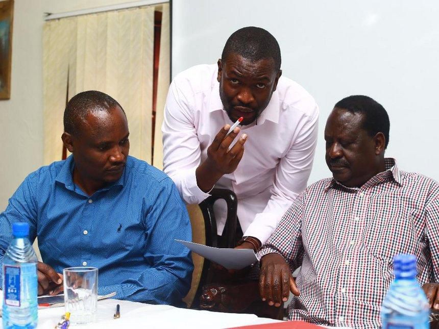 The late Raila Odinga listens as Edwin Sifuna briefs him. John Mbadi looks on