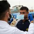 An Iraqi student shows an anti-government demonstrator how to wear a protective mask against the coronavirus during a rally in the southern Iraqi city of Basra
