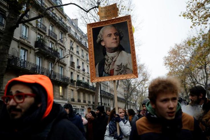 A protester holds a portrait of French President Emmanuel Macron painted as a royalty with a sign on top of it reading "14 May 2017 restoration of the monarchy"