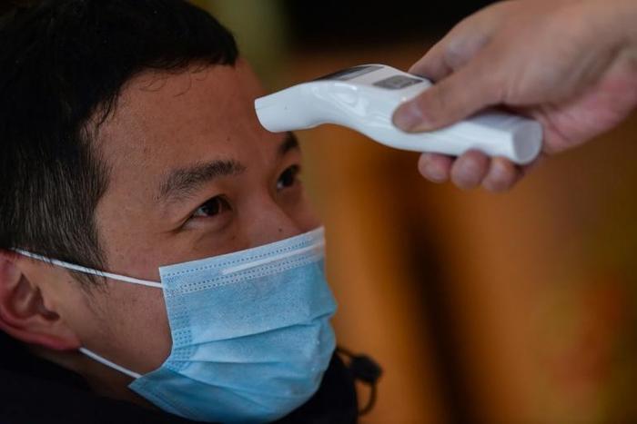 A hotel employee takes the temperature of a man who just arrived in the building in Wuhan