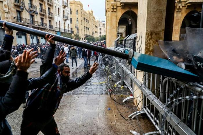 Anti-government protesters use a road sign to taunt security forces taking cover during clashes in the central downtown district in Beirut on Saturday
