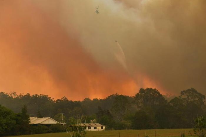 A helicopter drops water on a homestead as bushfires rage north of Sydney