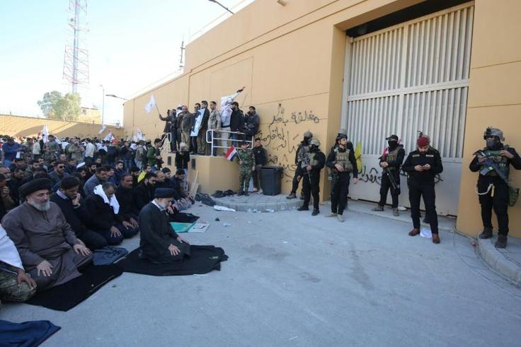 Iraqi security forces stand guard as protesters hold a prayer inside the walls of the US embassy in Baghdad's Green Zone
