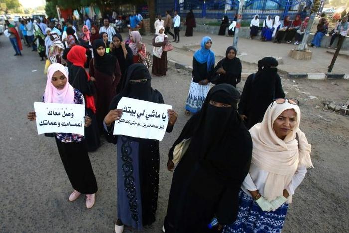 Sudanese protesters hold signs that read: "Take your uncles and aunts with you" and "You who's going home, give a lift to a couple of people"