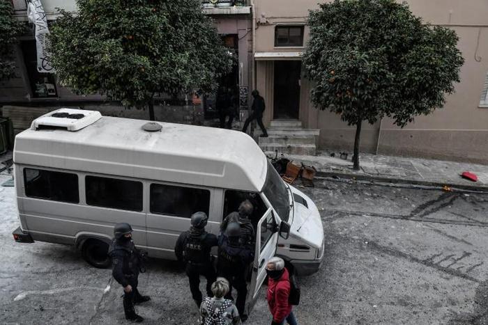 Police escort a detained man into a van after a raid on a "squat" in Koukaki, a central district of Athens in December 2019