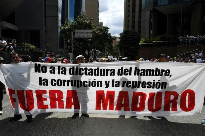 Supporters of Venezuelan opposition leader Juan Guaido hold a banner reading "Maduro Out" as they protest against President Nicolas Maduro in Caracas
